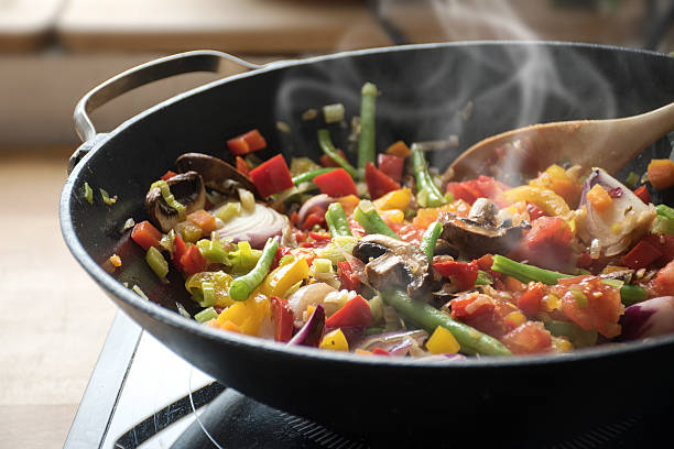 steaming mixed vegetables in the wok, asian style cooking stock photo