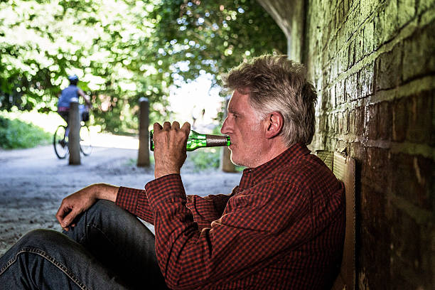 hombre adulto mayor sin hogar que duerme a la intemperie bebiendo de una botella de cerveza - brick wall homelessness wall begging fotografías e imágenes de stock