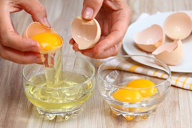 Woman hands breaking egg to separate  egg-white and  yolk Broken egg shells at the background egg yolk stock pictures, royalty-free photos & images
