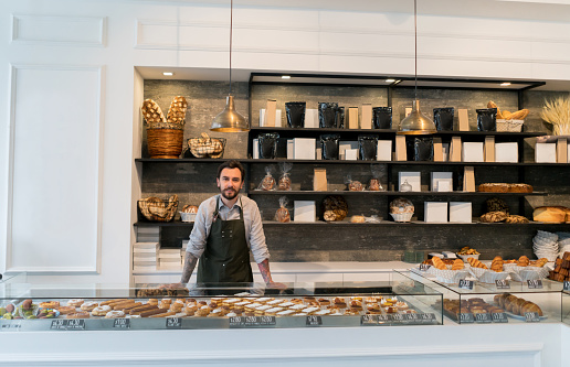 Business owner serving at a bakery shop and looking at the camera smiling - small business concepts