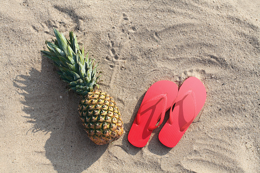 Summer photo pineapple and red flip flops lie on sand beach