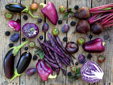 purple vegetables and fruits on wooden background - eggplant, peppers, beets, cauliflower, green beans, cherry tomatoes, plums, blackberries, basil, onion, black currants, cabbage