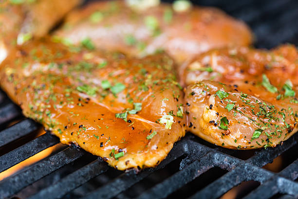 Raw marinated chicken breasts cooking on the BBQ grill.