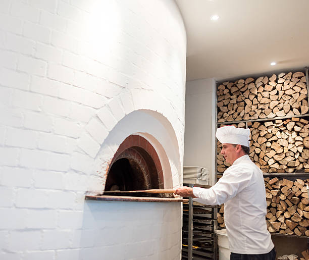 Chef making pizza in a wooden oven at an Italian restaurant - food and drinks concepts