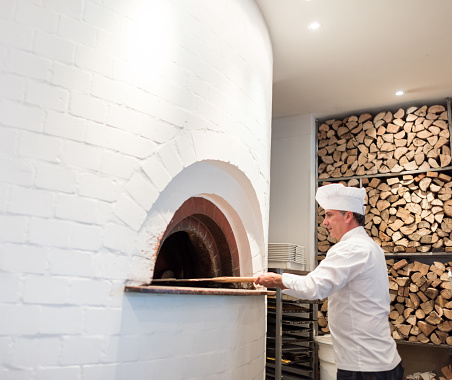 Chef making pizza in a wooden oven at an Italian restaurant - food and drinks concepts