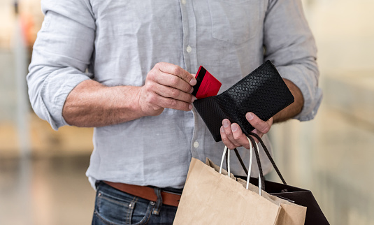 Unrecognizable shopping man putting credit card in his wallet while walking at the mall. Design on card is own design.