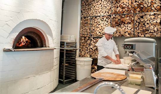 Chef working at an Italian restaurant making pizza kneading the dough - food and drinks concepts