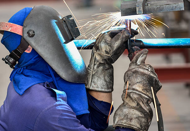 istock Welder in factory with protective equipment welding pipe 588618412