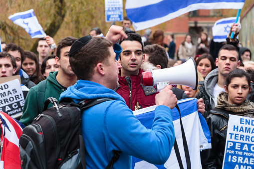 Birmingham, United Kingdom - November 28, 2012: Israeli student wearing blue hoody and backpack at Birmingham university demonstration for Israel holding a bullhorn while gesturing to a disinterested looking crowd of people holding signs and placards.