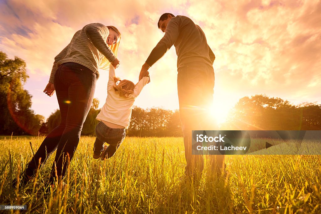 Parents hold baby's hands.  Happy family in park evening Happy family in the park evening light. The lights of a sun. Mom, dad and baby happy walk at sunset. The concept of a happy family.Parents hold the baby's hands. Family Stock Photo