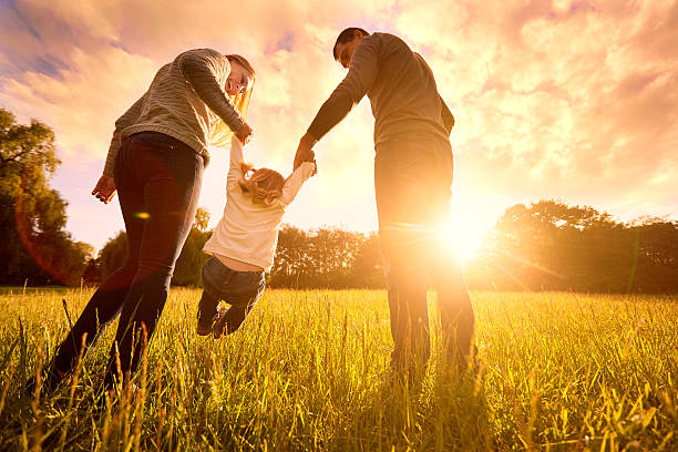 Parents hold baby's hands.  Happy family in park evening Happy family in the park evening light. The lights of a sun. Mom, dad and baby happy walk at sunset. The concept of a happy family.Parents hold the baby's hands. adoption stock pictures, royalty-free photos & images