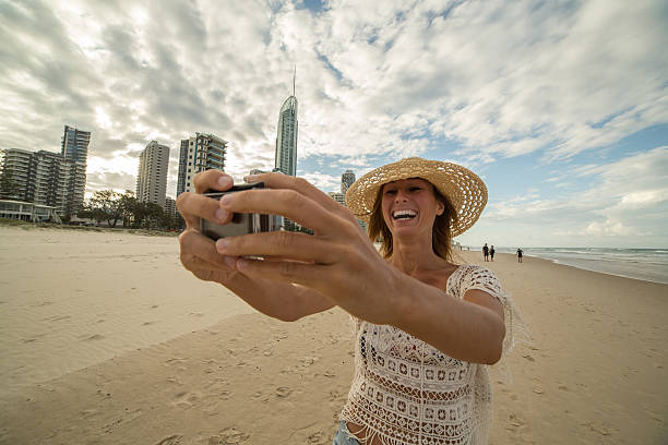 ビーチで白人の女性は、アクションカメラを使用して自分撮り肖像画を取ります - australia photographing camera beach ストックフォトと画像