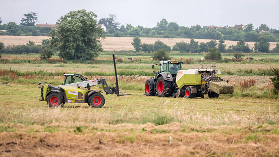Somerset, UK - July 9, 2016:  Farm vehicles at work in field harvesting hay. 