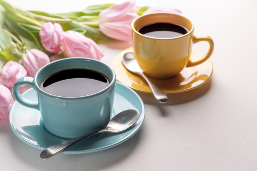 Blue and yellow cups of coffee with pink tulip on white background