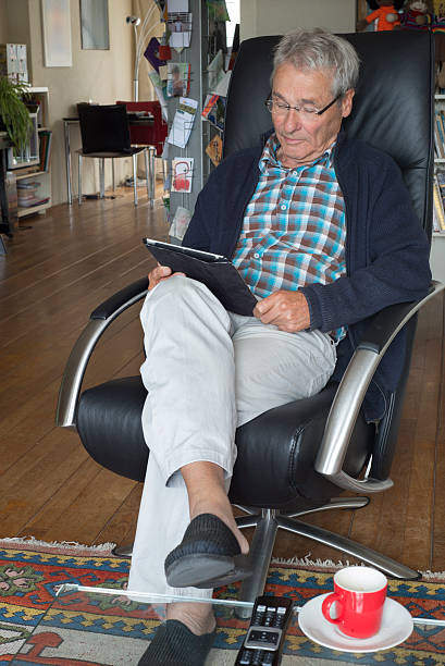 istock Elderly man reading his tablet in armchair with coffeecup 588967896