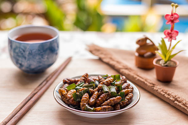 Fried insects - Wood worm insect crispy with pandan Fried insects - Wood worm insect crispy with pandan after fried and add a light coating of sauce and garnish Thai pepper powder with chopsticks, tea, brown cloth on wooden background, Select focus cambodia food stock pictures, royalty-free photos & images