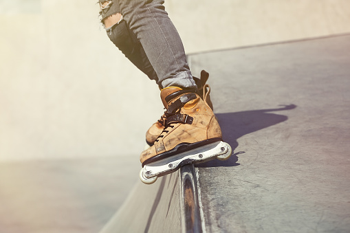 Feet of rollerblader wearing aggressive inline skates grinding on concrete ramp in outdoor skate park. Extreme sports athlete wearing roller blades for tricks and grinds