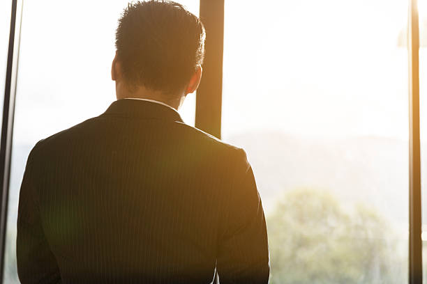 istock back of businessman in suit looking through office window 588982594
