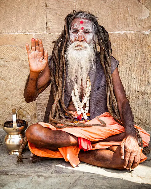 In Varanasi India, an Indian sadhu sitting on the ground is making a gesture with his hand, as a salute.