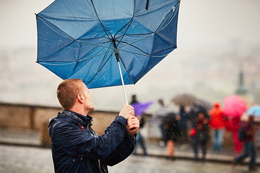 Rain in the city. Young man is holding blue umbrella during thunderstorm. Street of Prague, Czech Republic.