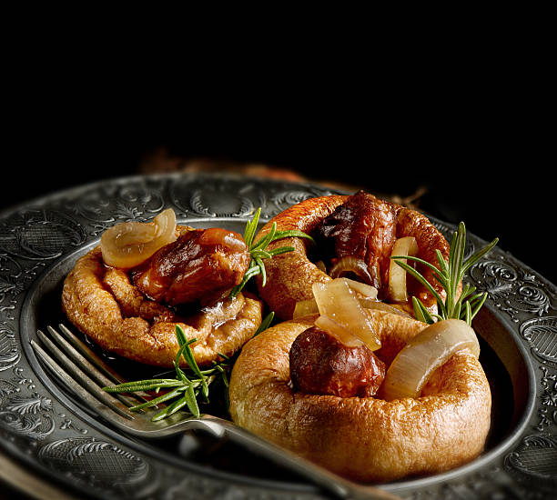 Toad in the Hole Classic English pub food dish of Yorkshire Pudding with pork sausages served with red wine onion gravy with a rosemary herb garnish. Perfect image for your bistro menu cover design. Copy space. pub food stock pictures, royalty-free photos & images