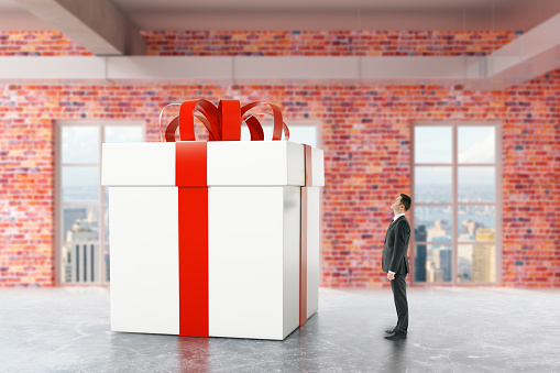 Businessman looking at huge present box in red brick interior with city view. 3D Rendering