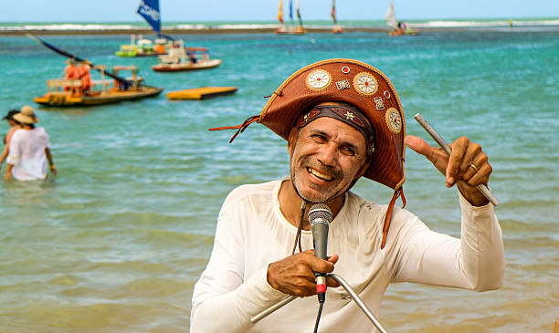 Beach singer in northeast Brazil Pernambuco, Brazil July 5, 2016: An unidentified singer in Chicken Beach with typical sail boats behind in Ipojuca City near barrier reef, northeast Brazil northeast stock pictures, royalty-free photos & images