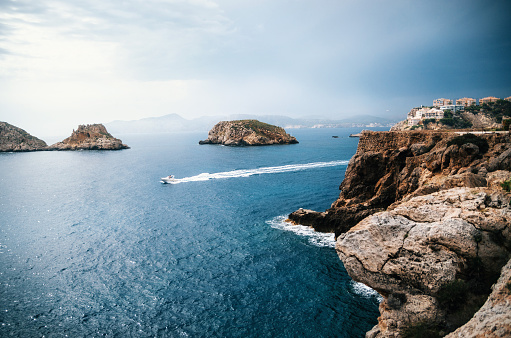 The yacht sails near the rocks of Santa Ponsa in the mediterranean sea before the storm, Mallorca Island, Spain