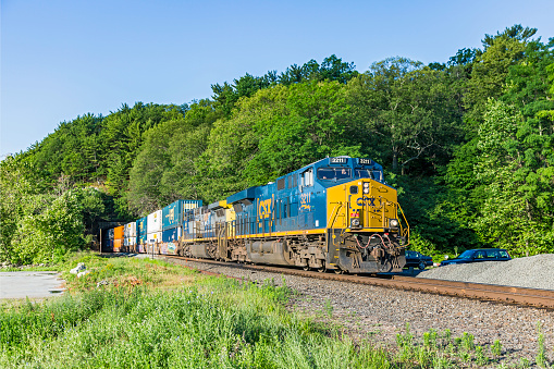 Fort Montgomery, United States - July 2, 2016: On a bright sunny summer day, CSX stack train Q161 (South Kearny - Chicago Intermodal) with GE locomotives 3211 & 444 exit the short tunnel near Bear Mountain, NY as it heads northbound.  CSX Transportation is a US Class I railroad serving major markets in the eastern United States.