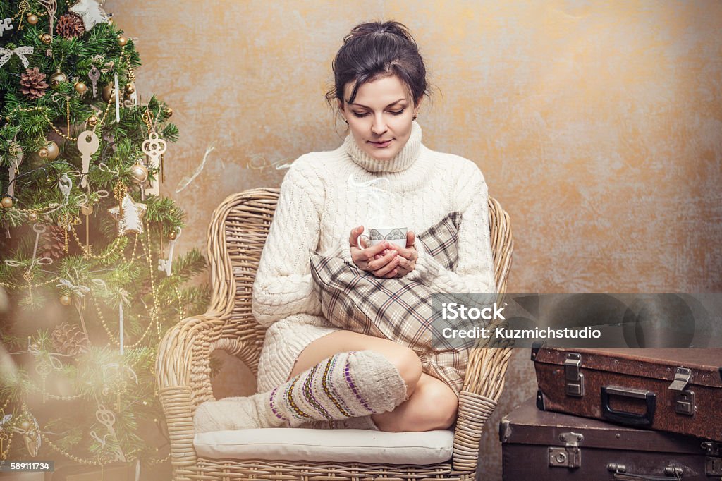 Beautiful woman drinking tea or coffee sitting in a chair Beautiful woman drinking tea or coffee sitting in a chair with pillows in the Christmas interior Adult Stock Photo