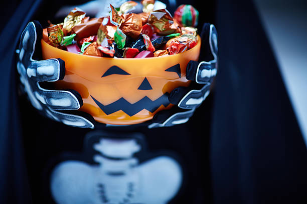 Treat, not trick Bowl with candies decorated as Jack O'lantern in the hands of Halloween character halloween candy stock pictures, royalty-free photos & images
