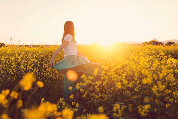 Dancing with flowers Rear view of a beautiful, russet young woman dancing in the middle of the flower meadow, surrounded by yellow flowers skirt photos stock pictures, royalty-free photos & images
