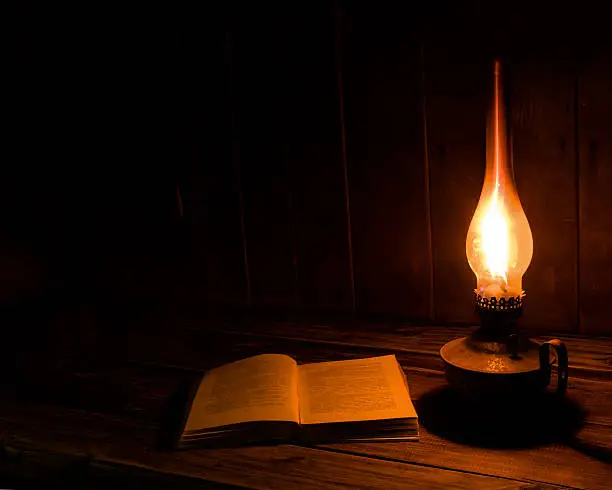 Old antique book opened with burning paraffin lamp near on the wooden table.