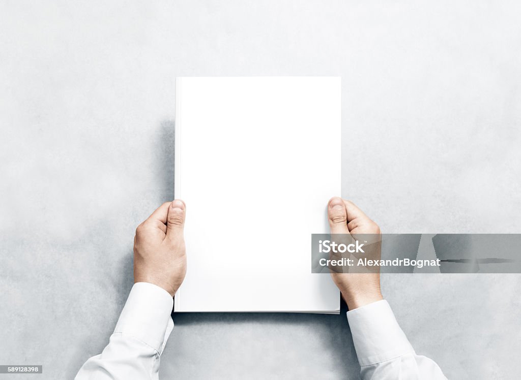 Hand holding white journal with blank cover mockup. Hand holding white journal with blank cover mockup. Arm in shirt hold clear magazine template mock up. A4 book softcover surface design. Paperback print display show. Closed notebook cover showing. Template Stock Photo