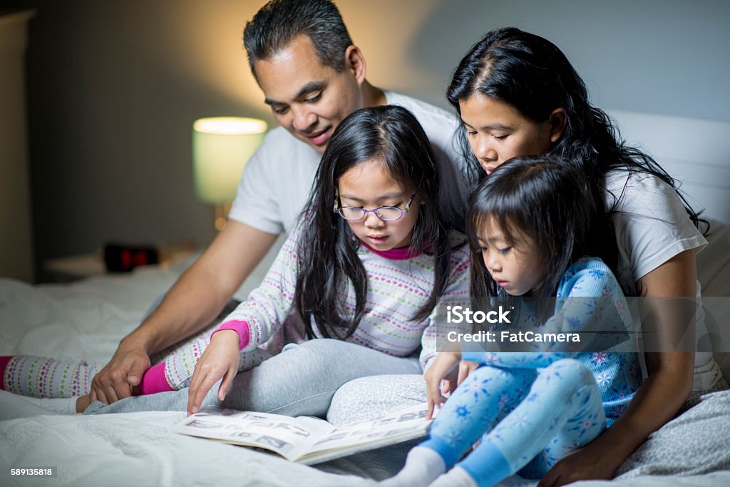 Reading a Storybook Before Bed A family of four are reading books together in bed before their daughters need to go to sleep. Reading Stock Photo