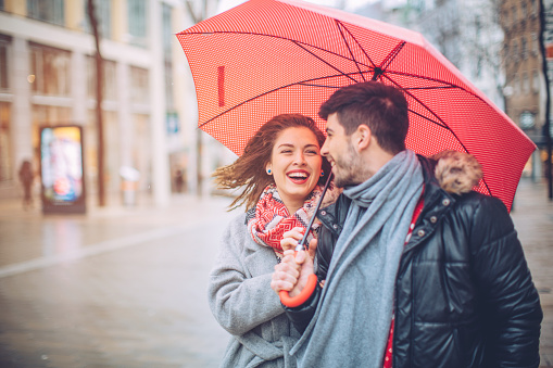 Couple walking on rainy autumn day. Wearing warm clohing and red umbrella.