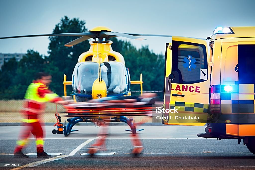 Emergency medical service Cooperation between air rescue service and emergency medical service on the ground. Paramedic is pulling stretcher with patient to the ambulance car. Helicopter Stock Photo