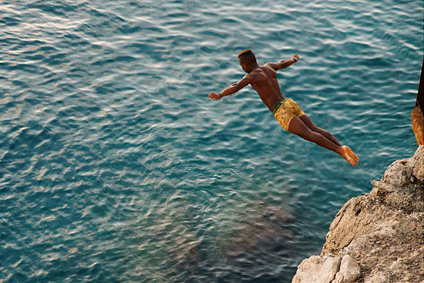 jovem saltar do penhasco no mar. - climbing men sea cliff imagens e fotografias de stock