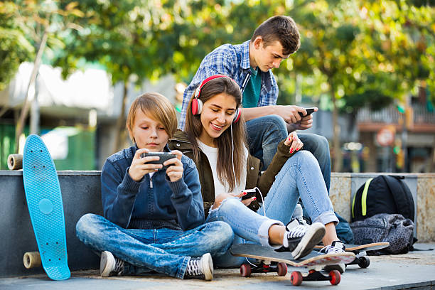 adolescentes activos jugando en teléfonos inteligentes y escuchando música - video game friendship teenager togetherness fotografías e imágenes de stock