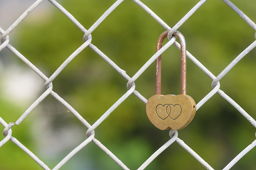 Closeup rusty heart shaped padlock locked on iron chain