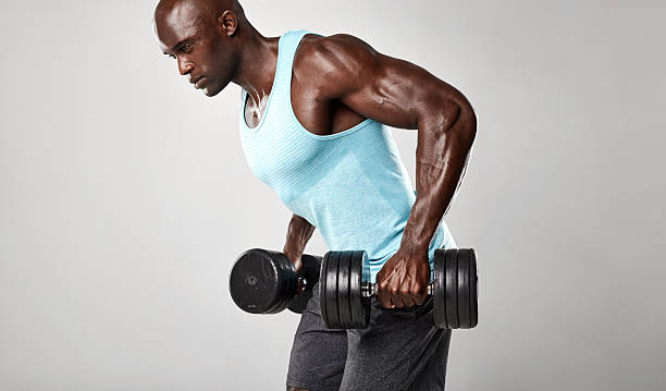 A fit Black athlete stretching his arms during a workout in a gym. Smiling male fitness trainer warming up, showing strength, health, and active lifestyle. Keywords: fitness, gym, stretching, athlete, workout, warm-up, trainer, active lifestyle, strong male model.