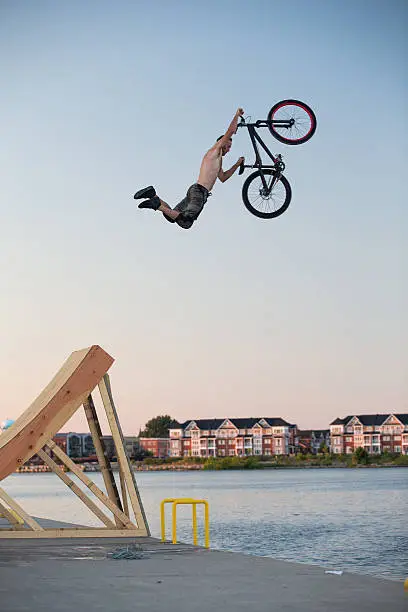 A man jumps a bicycle into the water from a pier off a wooden ramp.A man jumps a bicycle into the water from a pier off a wooden ramp.
