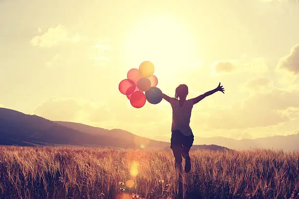 Photo of cheering young asian woman on grassland with colored balloons