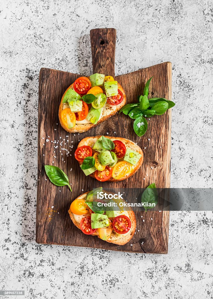 Bruschetta with tomatoes and avocado on rustic wooden cutting board Bruschetta with tomatoes and avocado on rustic wooden cutting board. Delicious snack or appetizer to wine Bruschetta Stock Photo