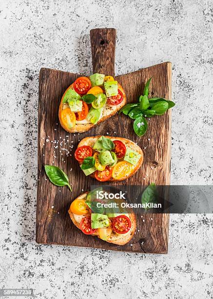 Bruschetta With Tomatoes And Avocado On Rustic Wooden Cutting Board Stock Photo - Download Image Now