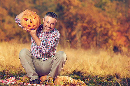 funny adult man in autumn day crafting Halloween Jack o'lantern and enjoying it.looking at camera.