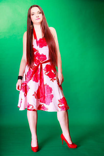 Summertime, vacation, holiday and date concept. Young long haired woman in floral outfit red high heels on green background in studio.