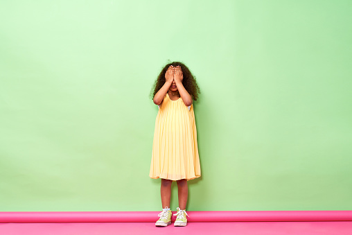 Little girl standing at wall and covering her eyes