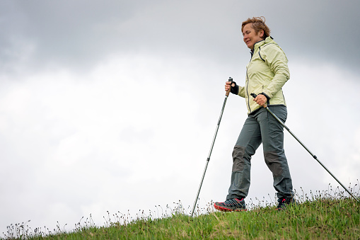 Mature woman Nordic walking with hiking poles on the Banjšice plateau in spring, Primorska region, Alps, Slovenia, Europe. Nikon D3x, full frame, XXXL.