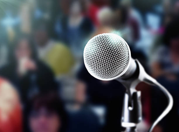 istock Brightly lit microphone with dark, defocused audience in the background 589540224